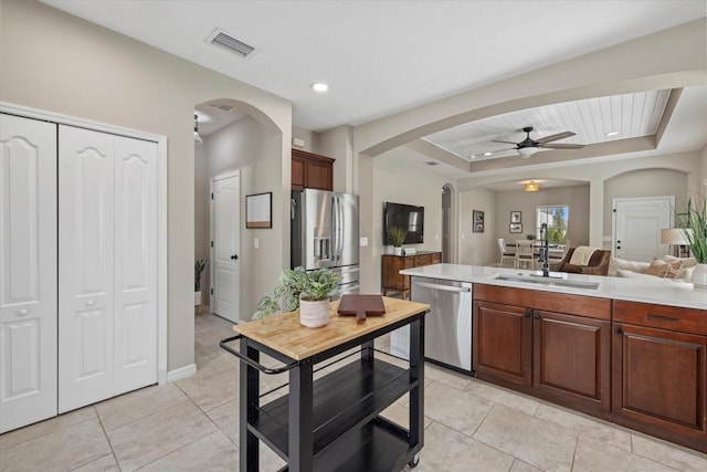 kitchen featuring stainless steel appliances, a raised ceiling, ceiling fan, light tile patterned flooring, and sink