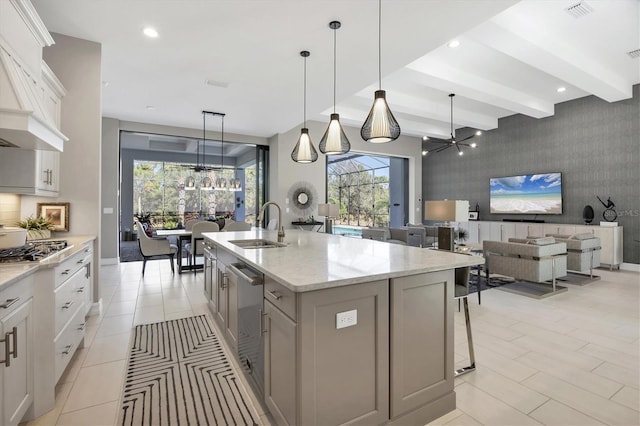 kitchen featuring an island with sink, beamed ceiling, sink, white cabinetry, and decorative light fixtures