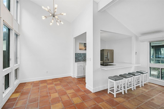 kitchen with high vaulted ceiling, backsplash, a wall mounted AC, stainless steel fridge, and white cabinets