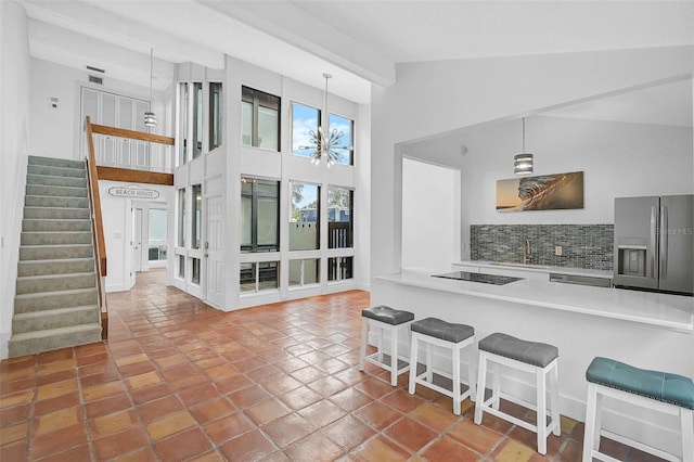 kitchen with high vaulted ceiling, sink, hanging light fixtures, decorative backsplash, and stainless steel fridge