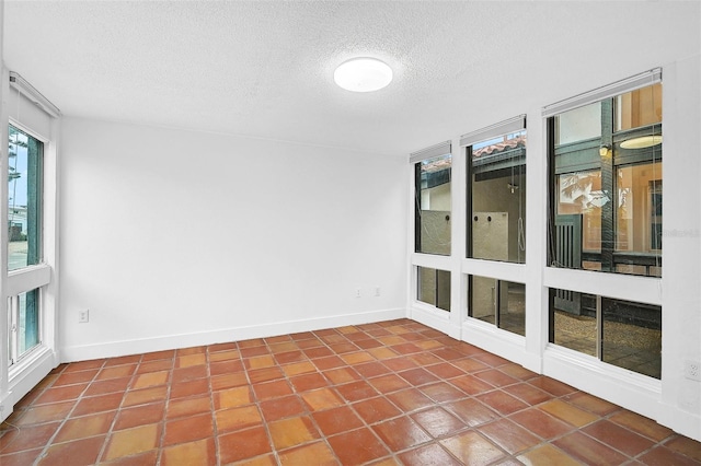 tiled empty room featuring a textured ceiling and baseboards