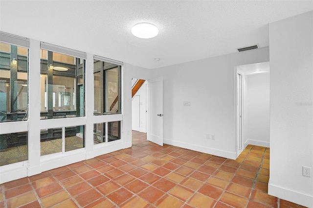 empty room featuring a textured ceiling, baseboards, visible vents, and tile patterned floors