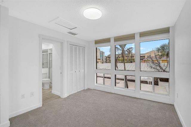 unfurnished bedroom featuring light colored carpet, visible vents, baseboards, a closet, and ensuite bath