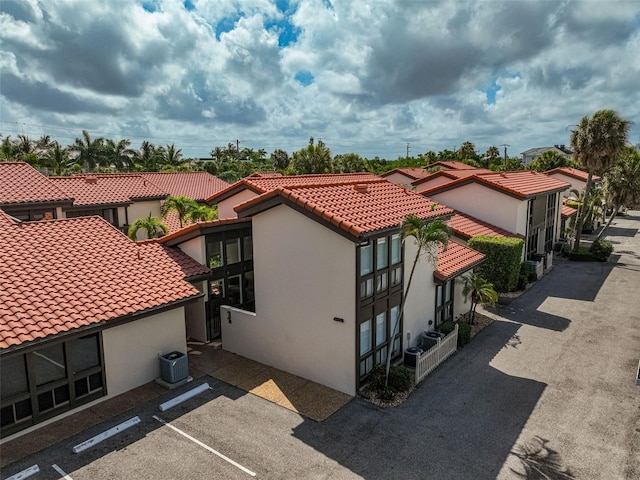 view of property exterior featuring uncovered parking, central AC, a tile roof, and stucco siding