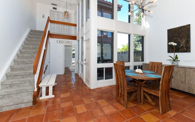 tiled dining area featuring a high ceiling, an inviting chandelier, and stairs