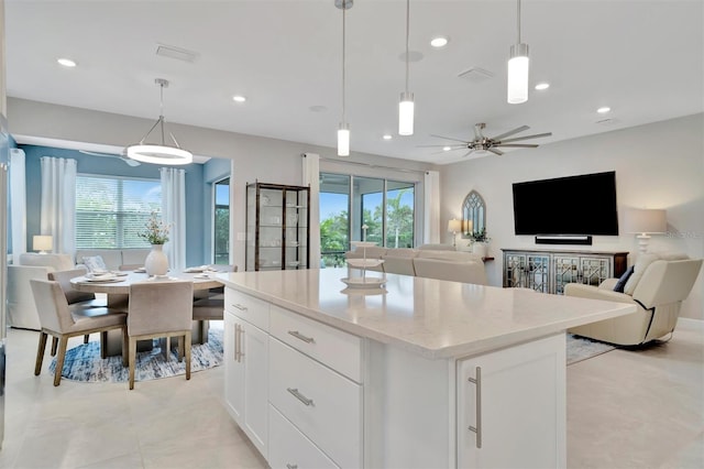 kitchen featuring ceiling fan, white cabinetry, a center island, and hanging light fixtures