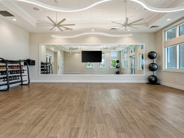 workout area with a tray ceiling, ceiling fan, and wood-type flooring