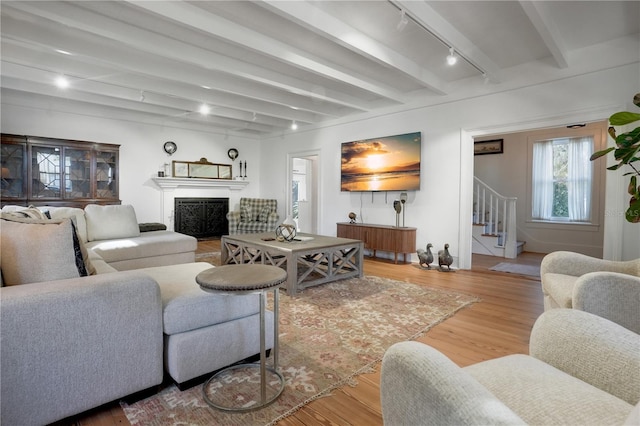 living room with light hardwood / wood-style flooring, track lighting, and beamed ceiling