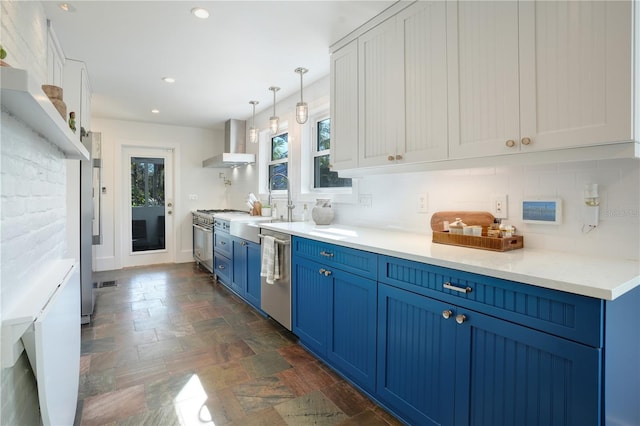 kitchen with appliances with stainless steel finishes, white cabinetry, wall chimney range hood, and blue cabinets