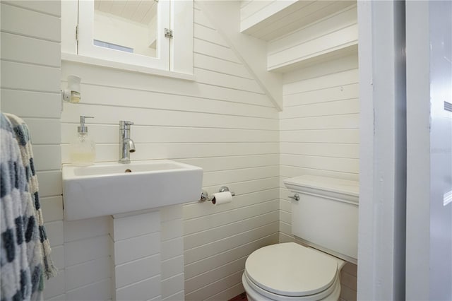 bathroom with toilet, wood walls, and sink