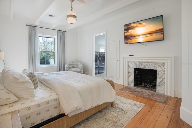 bedroom with a spacious closet, a closet, a high end fireplace, separate washer and dryer, and wood-type flooring