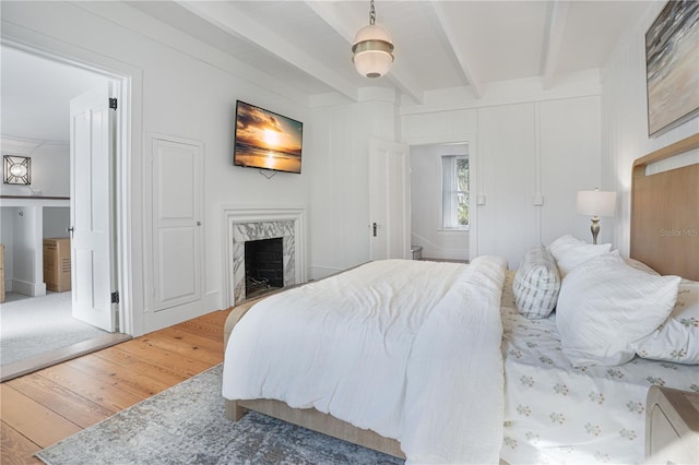 bedroom featuring wood-type flooring, ensuite bathroom, a fireplace, and beamed ceiling