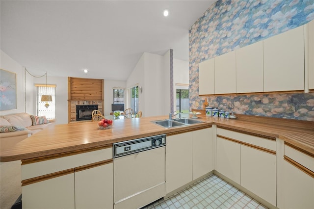 kitchen featuring white dishwasher, kitchen peninsula, sink, a brick fireplace, and butcher block counters