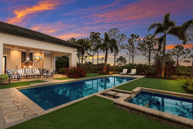 pool at dusk with an in ground hot tub, a patio, a yard, and an outdoor hangout area