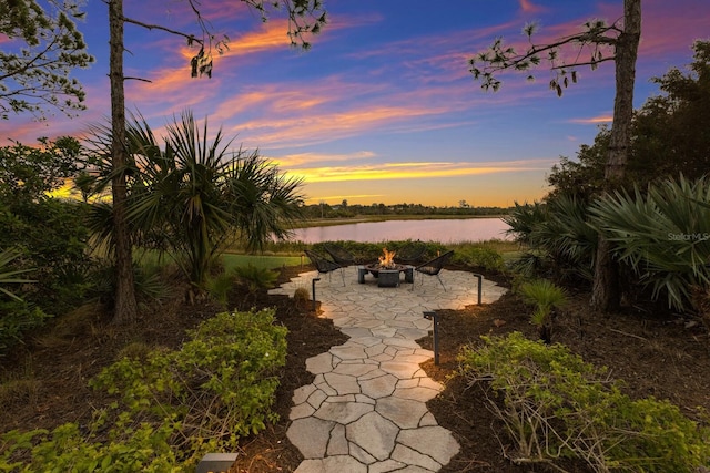 patio terrace at dusk featuring an outdoor fire pit and a water view