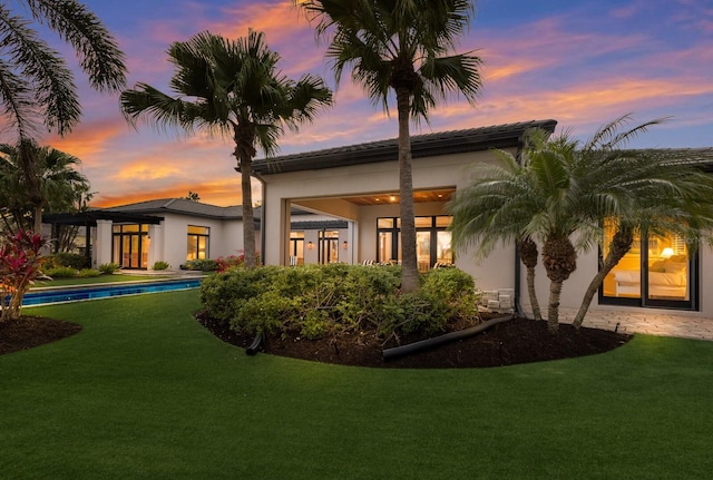 back house at dusk featuring a lawn