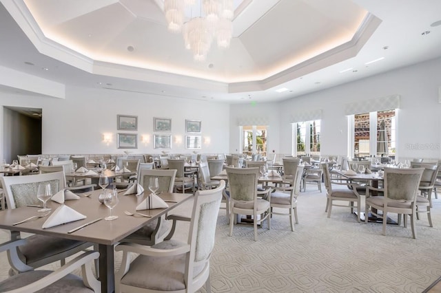 dining space with a high ceiling, light carpet, a raised ceiling, and a chandelier