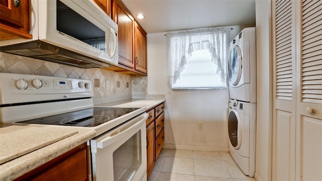 kitchen with backsplash, light tile patterned floors, stacked washing maching and dryer, and white appliances