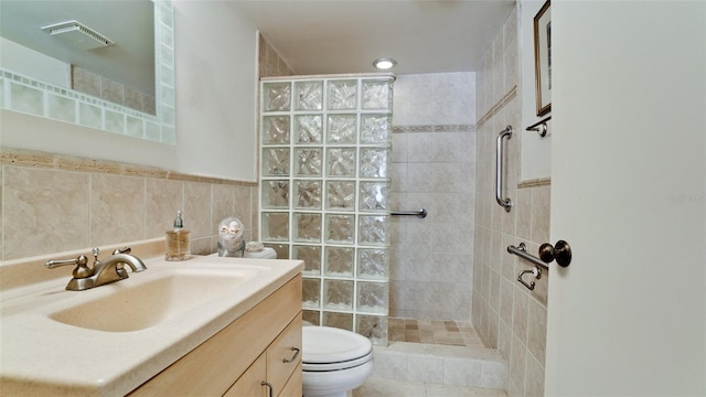 bathroom with a tile shower, vanity, toilet, and tile walls