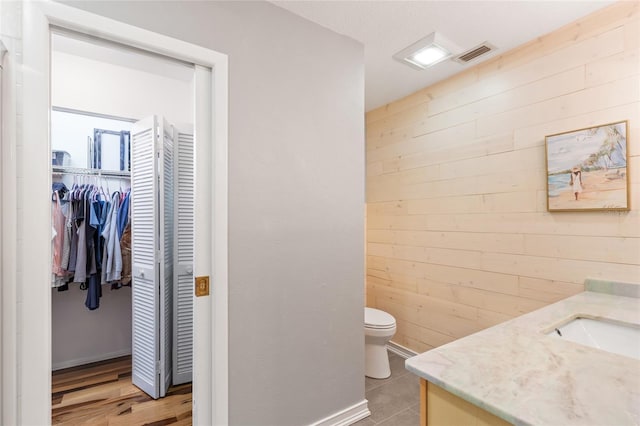 bathroom with wooden walls, vanity, and toilet