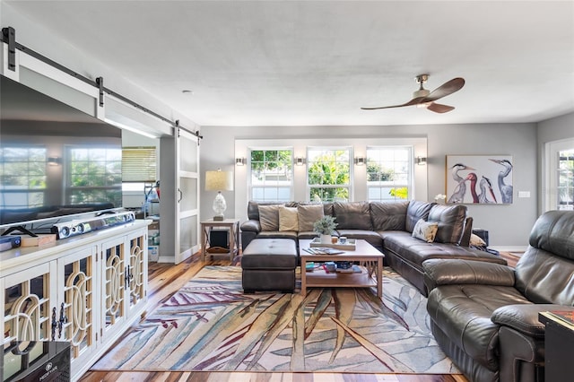 living room with light wood-type flooring, a barn door, and ceiling fan