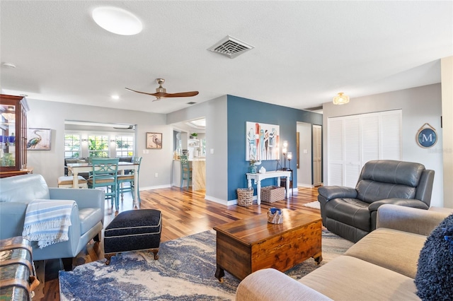 living room with ceiling fan, a textured ceiling, and light hardwood / wood-style flooring