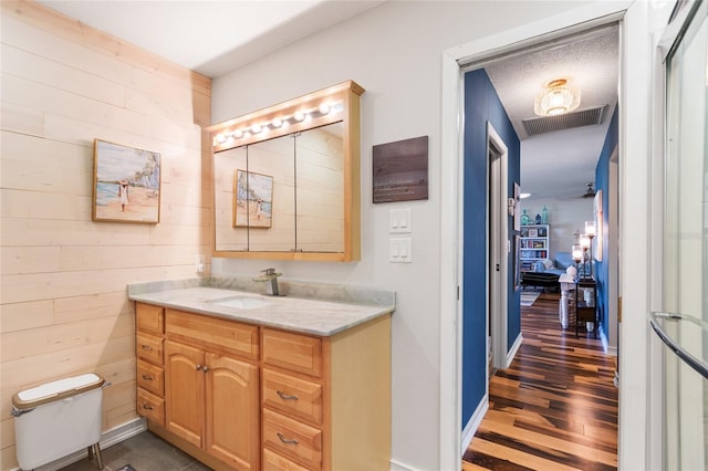 bathroom with vanity, wood walls, toilet, and a textured ceiling