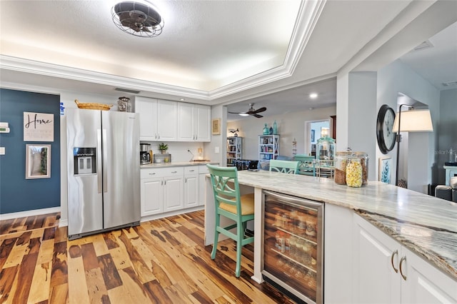 kitchen with light stone countertops, stainless steel fridge, a raised ceiling, beverage cooler, and white cabinetry