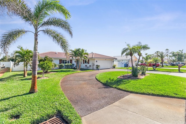 ranch-style house featuring curved driveway, a garage, fence, and a front lawn