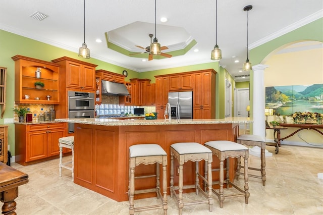 kitchen featuring ornate columns, pendant lighting, an island with sink, and stainless steel appliances