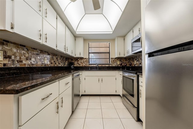 kitchen with dark stone counters, sink, appliances with stainless steel finishes, light tile patterned flooring, and white cabinetry