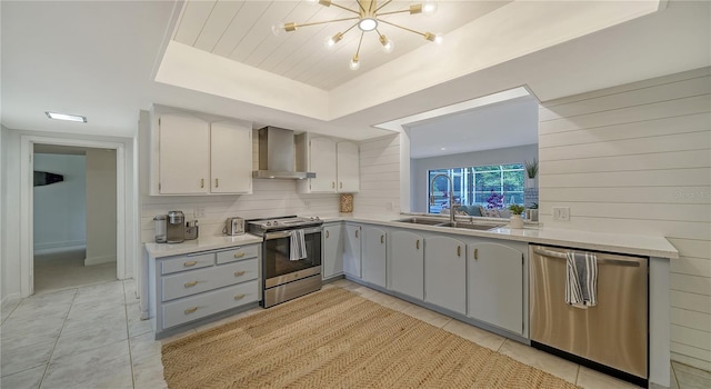 kitchen with light tile patterned flooring, wall chimney exhaust hood, gray cabinetry, appliances with stainless steel finishes, and decorative backsplash