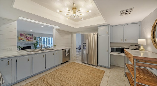 kitchen with a raised ceiling, sink, gray cabinetry, light tile patterned floors, and stainless steel appliances