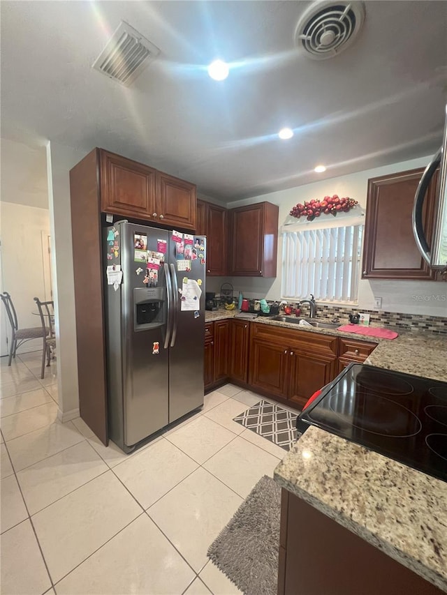 kitchen with sink, light stone counters, stainless steel fridge, stove, and light tile patterned flooring