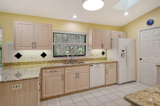 kitchen with vaulted ceiling with skylight, white appliances, light brown cabinets, sink, and light tile patterned floors