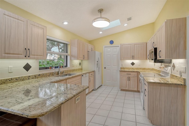 kitchen featuring white appliances, light brown cabinets, sink, light stone counters, and lofted ceiling with skylight