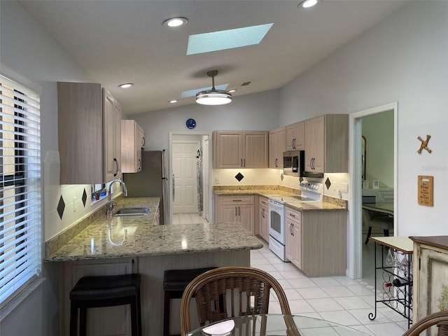 kitchen featuring lofted ceiling with skylight, a sink, light brown cabinetry, stainless steel appliances, and a peninsula