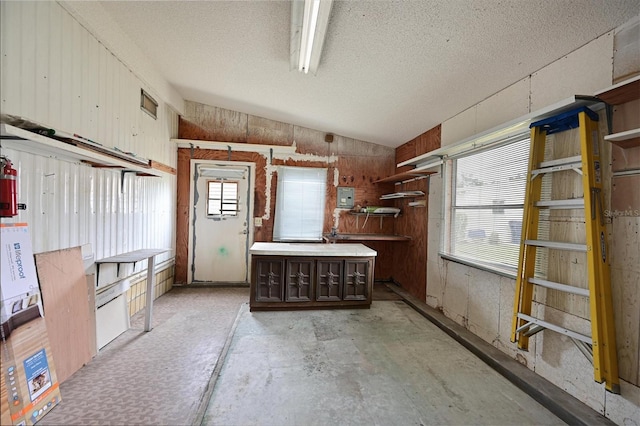 interior space featuring a textured ceiling, lofted ceiling, a kitchen island, wooden walls, and electric panel