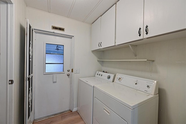 laundry area featuring cabinets, a textured ceiling, light wood-type flooring, and washing machine and clothes dryer