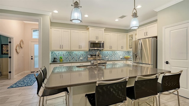 kitchen with stainless steel appliances, a center island with sink, white cabinets, and hanging light fixtures