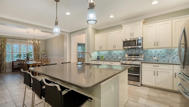 kitchen featuring decorative light fixtures, stainless steel appliances, a kitchen island with sink, and white cabinets