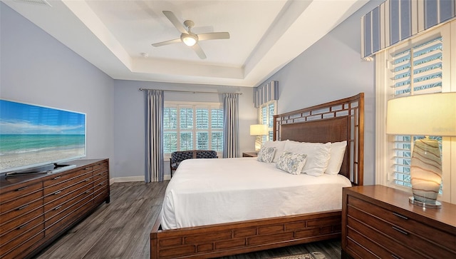 bedroom with dark hardwood / wood-style flooring, ceiling fan, and a tray ceiling