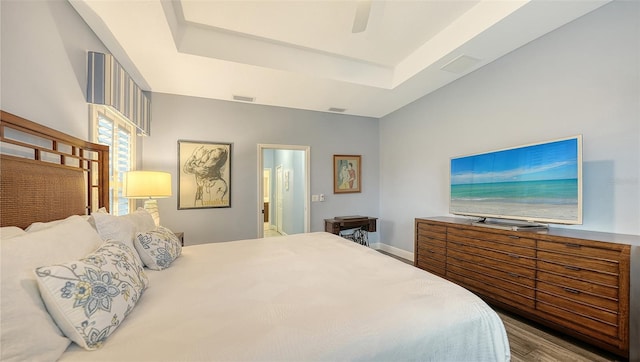 bedroom with ensuite bath, light wood-type flooring, ceiling fan, and a tray ceiling