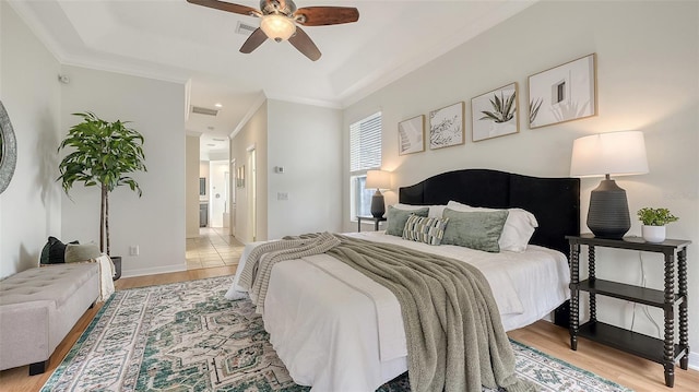 bedroom with visible vents, baseboards, light wood-style floors, ornamental molding, and ensuite bath