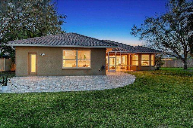 back of house featuring a patio, stucco siding, a lawn, fence, and a tiled roof