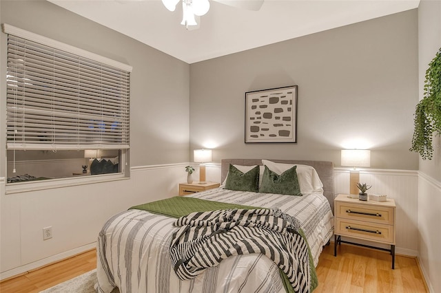 bedroom featuring a ceiling fan, a wainscoted wall, and wood finished floors