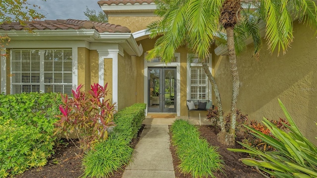 view of exterior entry with stucco siding, a tiled roof, and french doors