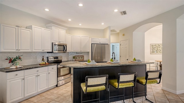 kitchen featuring arched walkways, stainless steel appliances, tasteful backsplash, visible vents, and white cabinetry