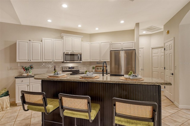 kitchen with a breakfast bar, tasteful backsplash, appliances with stainless steel finishes, light tile patterned flooring, and white cabinets