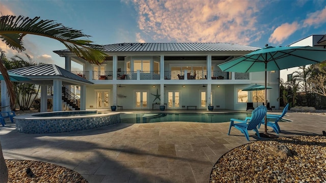 back house at dusk featuring a balcony, ceiling fan, a patio, french doors, and a swimming pool with hot tub